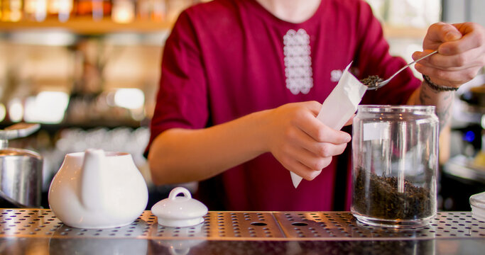 Tea shop. Preparing sachet drink. Barista pouring by spoon dried leaves in paper filter pack. Male worker measuring portion for herbal infuser. - Powered by Adobe