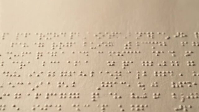 A macro, slightly angled shot reveals the intricate pattern of embossed Braille dots on a light, textured paper surface. The raised texture creates distinct shadows and highlights, emphasizing the tac