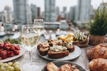 A group of friends celebrates a birthday on a rooftop as the sun sets. They enjoy tasty food and drinks while surrounded by a city skyline. The atmosphere is lively and festive