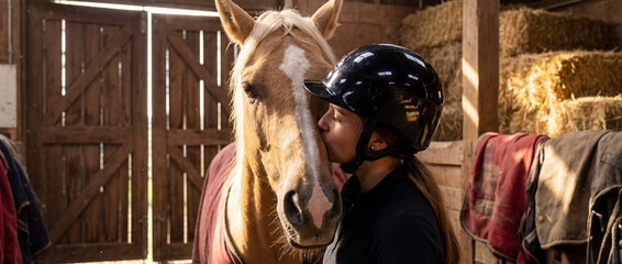 Kiss shared between rider and horse in stable during day
