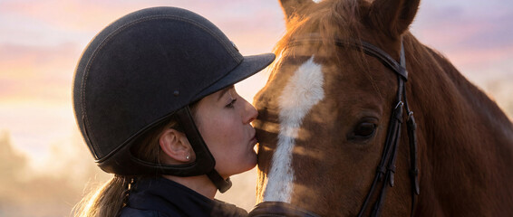 Woman kisses horse during sunset at a stable in the countryside