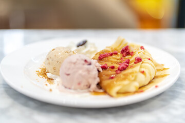 Soft focus dessert plate featuring folded crepes drizzled with syrup and topped with raspberries, served with two scoops of ice cream