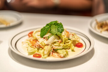 Shallow-depth shot of Thai style shrimp salad with lettuce, herbs, lemongrass and cherry tomatoes topped with fresh mint leaves