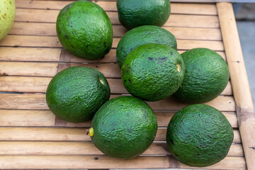 A group of fresh green avocados with rough skin placed on a bamboo slat table.