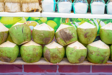 Fresh young coconuts with green husks trimmed into diamond shapes displayed on a shelf for sale.