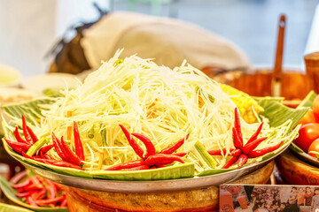 Pile of fresh shredded green papaya with red chilies for making traditional Thai spicy salad.