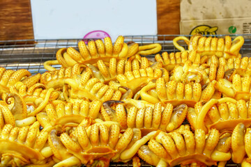 Pile of yellow grilled squid eggs or roe on rack at street food market.