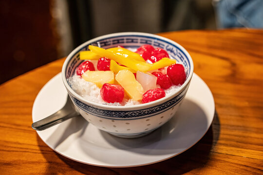 A bowl of Thai Red Ruby dessert or Tub Tim Krob with jackfruit and ice in coconut milk on a wooden table.