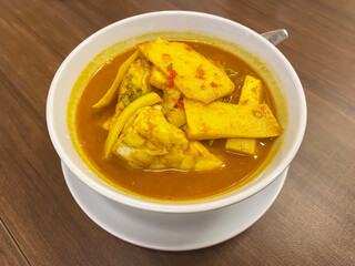 Southern Thai style spicy yellow curry with fish and bamboo shoots served in white round bowl.