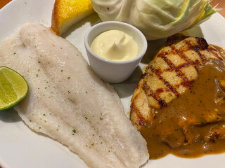 A combo platter featuring a grilled chicken steak with gravy and a white fish fillet, served with salad, toast, and mayonnaise.