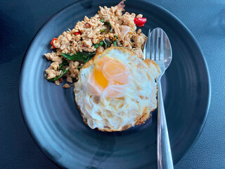 A classic Thai dish of spicy basil minced pork stir-fry served over rice with a crispy fried egg on a black plate.