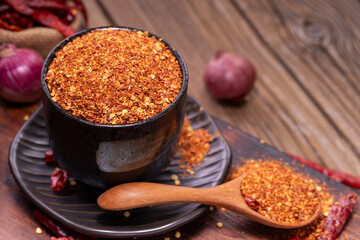Chili powder in black bowl and wooden spoon with garlic, shallots, spicy spice mix. Asian food ingredients arranged on wooden table. Top view.