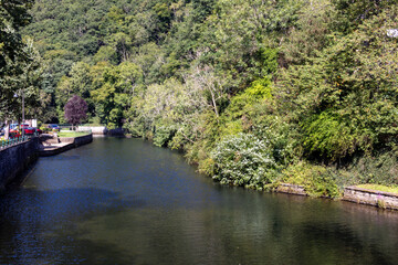 Obraz premium Esch-sur-Sure, Wiltz, Grand-Duche de Luxembourg, September 07, 2025, Calm waterway around lush banks, Idyllic waterway winding through peaceful landscapes with nearby strolling route