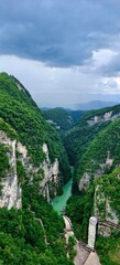 Zhangjiajie Grand Canyon in China, a lush, verdant gorge with dramatic cliffs and a turquoise river winding through, leading to the famous Glass Bridge landmark under a dramatic, cloudy sky