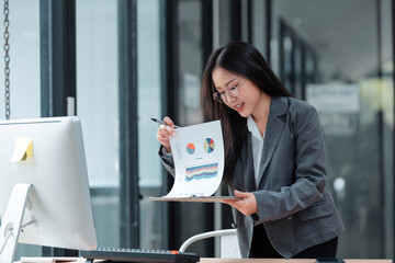 Young professional businesswoman presenting business charts and statistics, explaining report findings to colleagues in a modern corporate setting