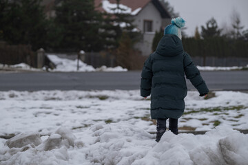 Small Child Walking on Snow Near Road in Winter Suburb