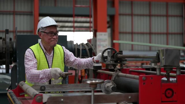 Asian industrial worker inspecting stack of corrugated metal roofing sheets in factory warehouse. Male employee checking construction material quality for manufacturing and building supply concept.