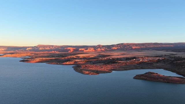 Drone footage moves smoothly along the dramatic red rock cliffs and clear blue water of Abiquiu Lake, New Mexico. This striking high desert landscape is evocative of the Southwest mesas.
