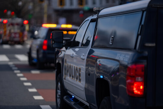 Police vehicle responds to alert. Security units monitor the street. Emergency lights flash in traffic. Law enforcement ensures protection. Capitol area stays under control.