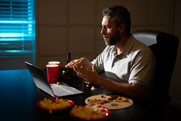 Businessman eats a late-night snack while working on laptop. A tired employee using laptop on late-night overtime. Business man overworked into the night. Freelancer eat pizza late at night.