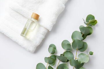 白いタオル、ユーカリの葉、竹の蓋付きアロマオイルの小瓶の俯瞰図 / Overhead view of a white towel, eucalyptus leaves, and a small bottle of aroma oil with a bamboo cap