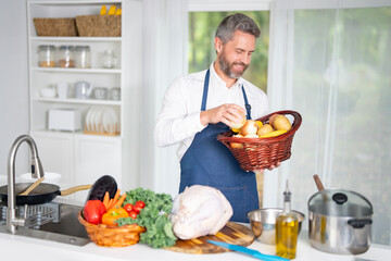 Cook cooking vegetables in kitchen. Chef in apron prepares healthy meal in modern kitchen. Cook with vegetables in white kitchen. Cook prepares breakfast with veggies at home kitchen.