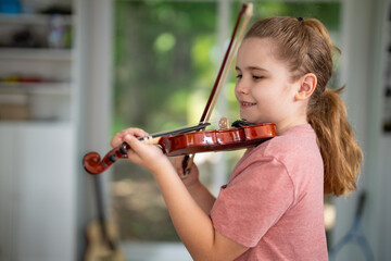 Kid playing violin at home. Child practicing classical music indoors. Young violinist. Kid with musical instrument. Young musician learning music on violin. Child practicing acoustic violin indoors.