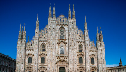 Duomo di Milano cathedral facade with blue sky background. Beautiful Gothic architecture facade of Milan Duomo Cathedral in Italy. Duomo di Milano. Front view of Milan Cathedral Duomo.