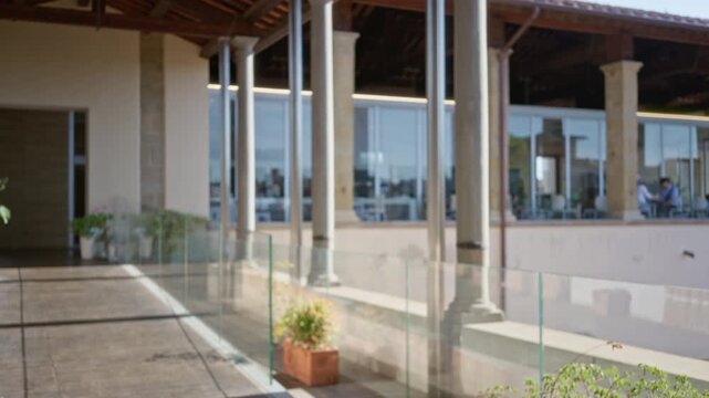 Terrace balcony with stone columns, glass balustrade and potted plants, sunlit floor and distant cafe windows in soft defocused bokeh outdoor; background backdrop copyspace template.