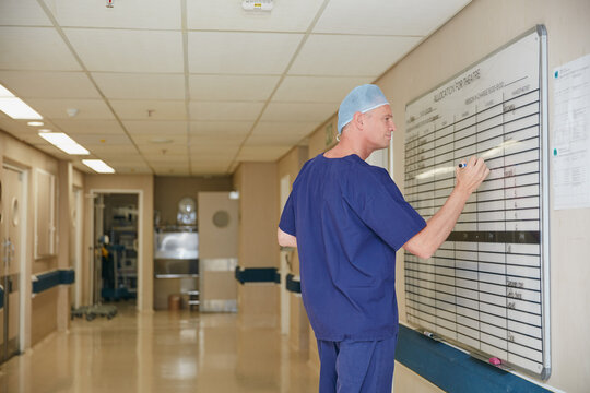 Fototapeta Surgeon, whiteboard and writing in hospital with schedule, operation theater roster or organization. Mature man, doctor and notice board in clinic with healthcare calendar, surgery timetable or plan.