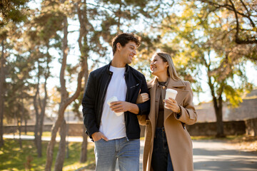 Young couple enjoys a sunny walk in the park with coffee on a beautiful autumn day