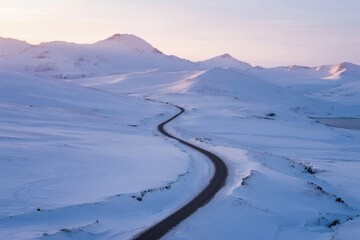 A winding road cuts through a snow-covered landscape with distant mountains under a soft twilight sky.
