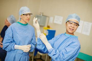 Woman, surgeon and team with gloves, prepare and ready for job in operating room at hospital. People, doctors and scrubs with ppe, gear or medical staff with healthcare services at trauma clinic