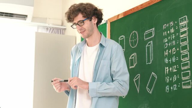 Caucasian teacher looking at student while standing at blackboard. Low angle camera of professional instructor teaching and explain math theory while answer question from diverse student. Pedagogy.