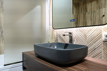 Sleek black vessel sink on wooden vanity, surrounded by textured tile walls, creating a modern, minimalist bathroom design.