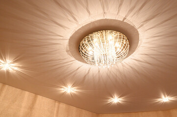 Ornate crystal chandelier with intricate, radiant design, surrounded by recessed ceiling lights, creating a warm, elegant ambiance