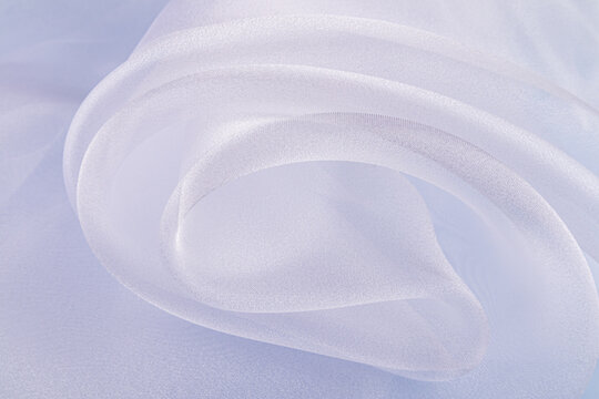 Beautiful large silk flounces of transparent organza. white air waves of fabric. Front view of soft waves of snow-white organza on a blue background.