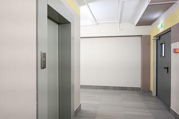 Hallway with elevator, tiled flooring, neutral wall colors, and minimal decor, creating a clean, functional and contemporary commercial or institutional space