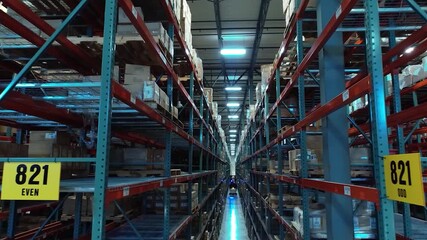 A cinematic drone shot flying down a tall warehouse aisle, smoothly tracking a forklift moving between shelves of stored packages. - Powered by Adobe