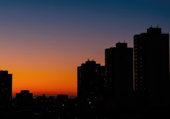 Naklejka premium Dramatic urban profile visible at twilight. Tall structures form a deep black silhouette against the vibrant, colorful background of the fading evening sky ,ambient ,financial ,tower
