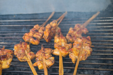 Grilled chicken on bamboo skewers over charcoal surrounding with smoke