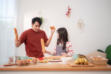 A father and daughter playfully sword-fight with baguettes in the kitchen