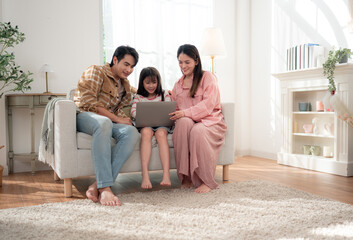 A family sits together on the sofa watching something on a laptop