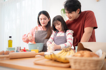 A family helping their daughter roll dough together in the kitchen, enjoying a fun baking moment