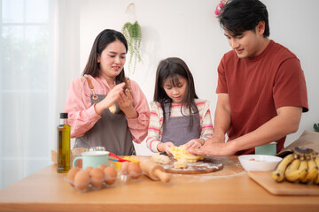 A family helping their daughter roll dough together in the kitchen, enjoying a fun baking moment