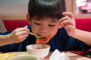 Cute Asian child eating salmon sushi in cozy restaurant setting, authentic lifestyle food scene