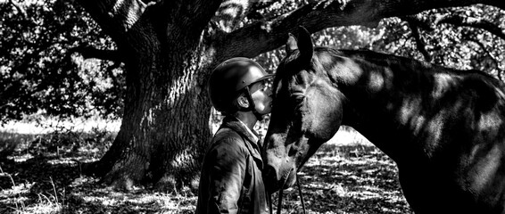 Soldier and horse share a moment under trees in bright sunlight