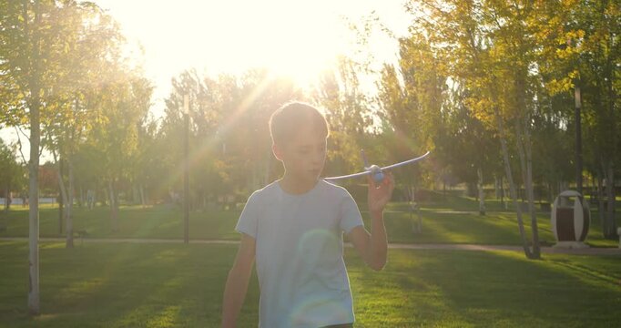 Child boy runs with toy airplane in summer park. Sunset light creates warm outdoor mood. Child imagines flight and freedom. Toy airplane inspires dream play. Active child energy. Joyful and happy kid