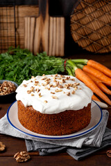 Carrot cake with cinnamon, walnuts and cream cheese frosting on a plate on a dark wooden background. Rustic style. Copy space.