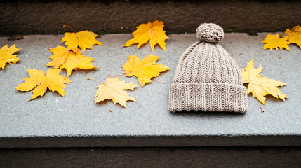 Beanie and yellow autumn leaves on the edge of a stone step, creating a cozy autumn scene. Perfect for warm weather during the fall season. Hat's soft texture makes it inviting